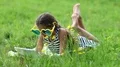 Girl in big sunglasses in the shape of hearts with tablet pc lies on green grass HD Footage