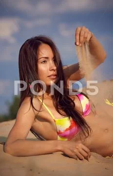 A girl in a bikini lies on sand Stock Photos