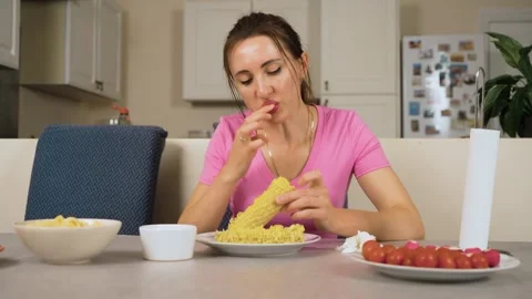 Girl biting corn cob during meal at kitchen table Stock Footage 328372193