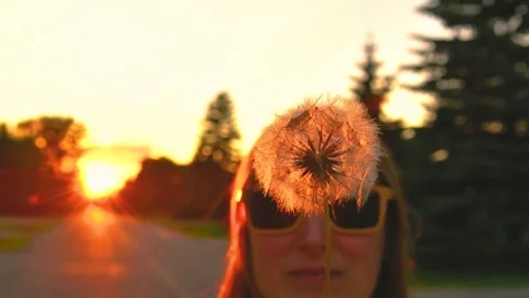 Girl blowing dandelion seeds in urban street at sunset Stock Footage