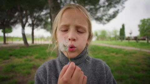 Girl blowing empty dandelion stem facing the camera in park Stock Footage 337814456