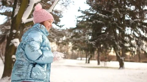 Girl in a blue down jacket and a pink hat throws a snowball at her father Stock Footage 101685747