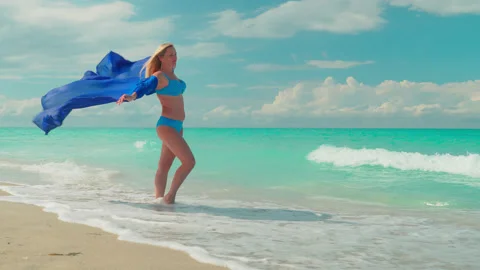 Girl in a blue pareo develop on the wind and stand along the shore of the turquo Stock Footage 172048745