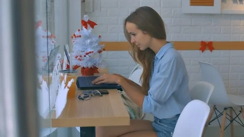 Girl in Blue Types on Computer at Counter by Window Stock Footage 86797651