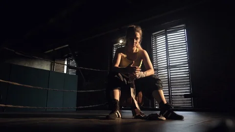 Girl the boxer pulls on her hand a protective tape sitting in a darkened room Stock Footage 112940701