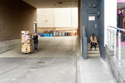 Girl on break sitting on steps using a phone with another woman pushing a tro Stock Photos