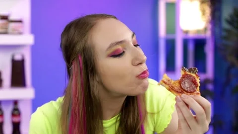 A girl with bright hair eats a slice of pizza at home Stock Footage 161875574