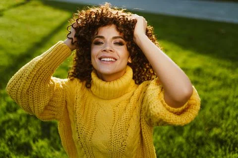 A girl in a bright yellow sweater shaggy her brown curly hair against a Stock Photos