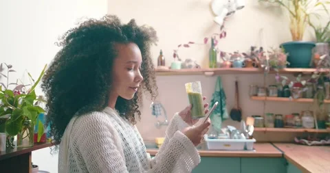 Girl browsing on social media while enjoying her green smoothie in her kitchen Stock Footage 198360508