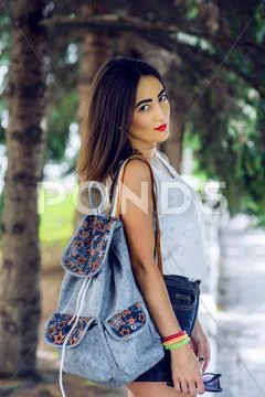 Girl brunette in summer in the park with a backpack resting in shorts and white Stock Photos