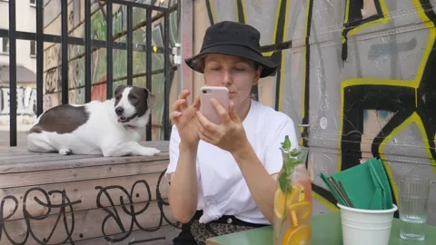 Girl in a bucket hat using her smartphone while waiting in a cafe with pretty Video stock 138138799