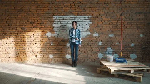 Girl Builder on brick wall background dancing and paints the wall with white Vídeo Stock 89710079