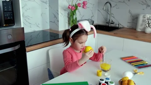 Girl with bunny ears paints Easter eggs at home in the kitchen.Happy Easter. Stock Footage 172097929