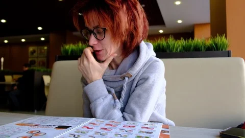 The girl in the cafe at the big window looking at the menu Light skin. glasses o Stock-Footage 129068044