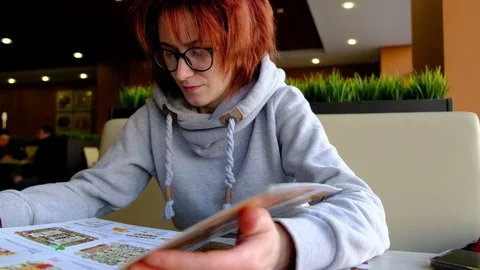 The girl in the cafe at the big window looking at the menu Light skin. glasses o Vídeos de archivo 129069060