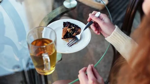 A girl in a cafe at a table sits drinking tea with a cake. Stock Footage 167858941
