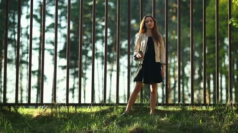 Girl in casual clothes smokes an electronic cigarette  near a fence. Stock Footage 109042553