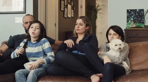 Girl changing channels while watching tv with family in living room Stock Footage 63861366