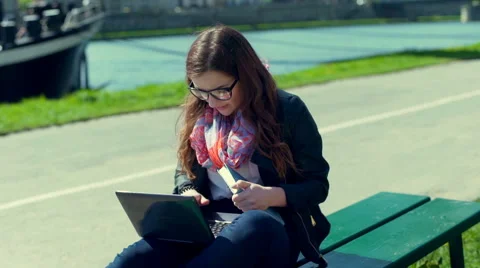 Girl checking something in the book and typing on laptop on boulevard Stock-Footage 66524689