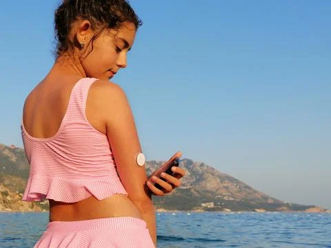 Girl checks glucose level  with CGM device before enters the sea. Stock Photos