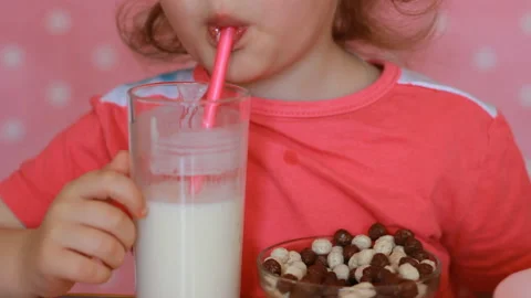 Girl child eats breakfast flakes and drinks a milk drink from a straw. Close-up Stock Footage 89525591