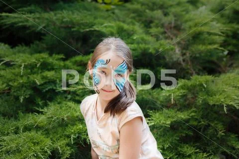 Girl child outdoors in park with butterfly face painting Stock Photos