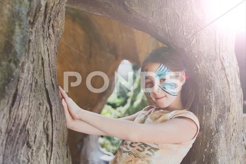 Girl child outdoors in tree with butterfly face painting Stock Photos