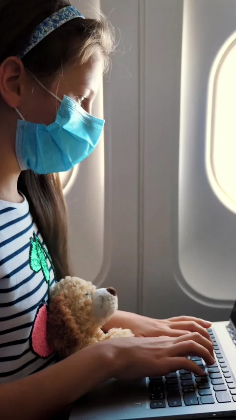 Girl, child in protective mask uses laptop while travelling by airplane. sitting Stock Footage 316128341
