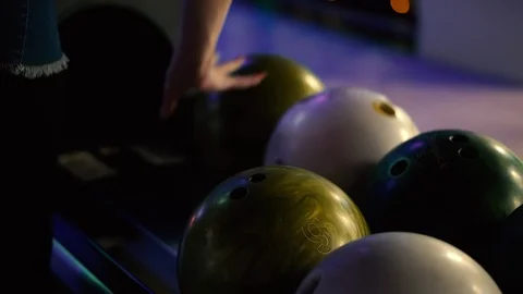 A girl chooses a ball before throwing while playing bowling club. Women's hands Stock Footage 101178897