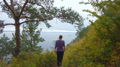 Girl climbs down the path on the steep slope of the coast in the autumn Stock Footage 122798471