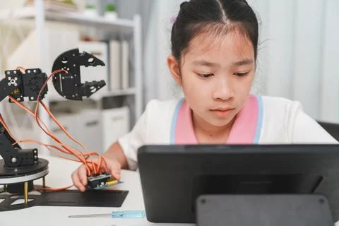 A girl codes a robot with a tablet. Programming, STEM, and e-learning concept Stock Photos