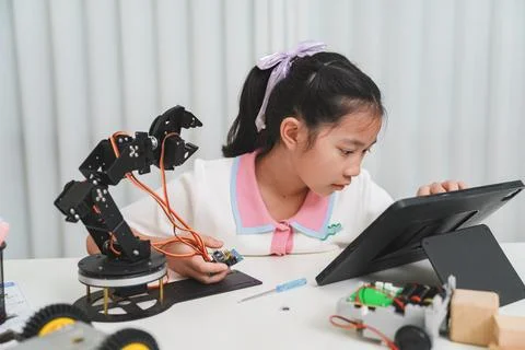 A girl codes a robot using a tablet. E-learning, STEM, and programming concep Stock Photos