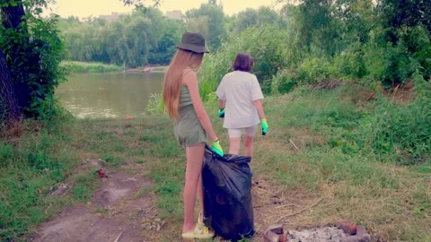 Girl collecting plastic litter under shadow of large tree Stock Footage 340463587