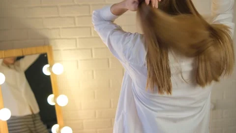 A girl combs her long smooth golden hair in a studio, salon. In front of the mir Stock Footage 148991755