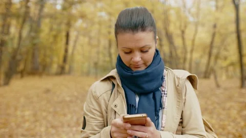 Girl communicates through a social network on a smartphone in an autumn park Stock Footage 219615230