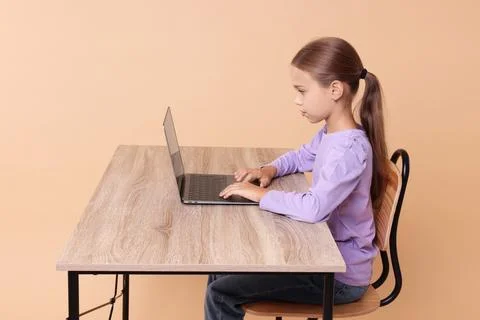 Girl with correct posture using laptop at wooden desk on beige background Stock Photos