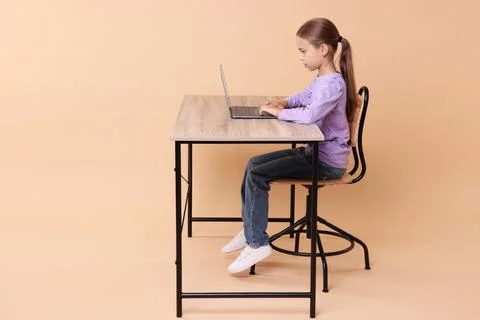 Girl with correct posture using laptop at wooden desk on beige background Stock Photos