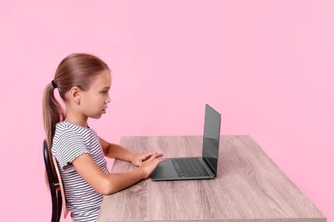 Girl with correct posture using laptop at wooden desk on pink background Stock Photos