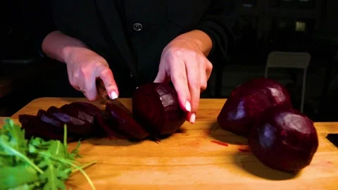 A girl cuts beets into thin slices on a wooden board with a knife Stock Footage 220684824