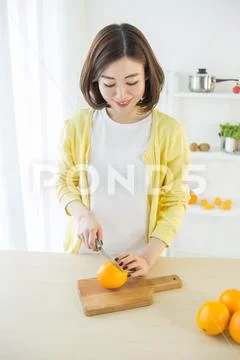 Girl cutting orange with the knife, on a wooden plate Stock-Fotos