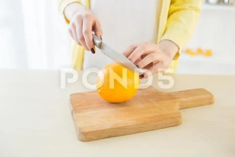 Girl cutting orange with the knife, on a wooden plate Stock-Fotos