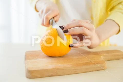Girl cutting orange with the knife, on a wooden plate Stock-Fotos