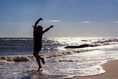 The girl dancing and bouncing on the seafront in the background of the sunset Stock Photos