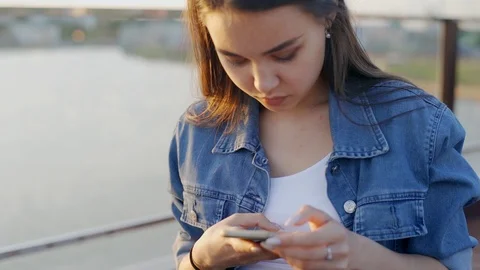 The girl in the denim jacket is typing a text message on the smartphone. The Video stock 110752775