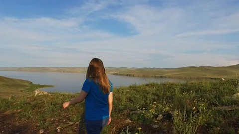 The girl descends down the path to the water. Green hills of Ogoi Island, Lake Stock Footage 128409820