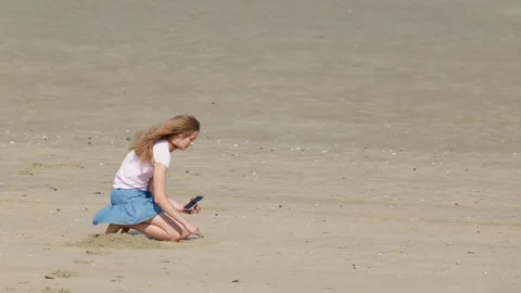 Girl Digging in Beach Sand While Holding a Smartphone Video stock 347451180