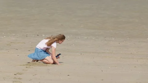 Girl Digging in Beach Sand While Holding a Smartphone Slow Motion Video stock 347585134