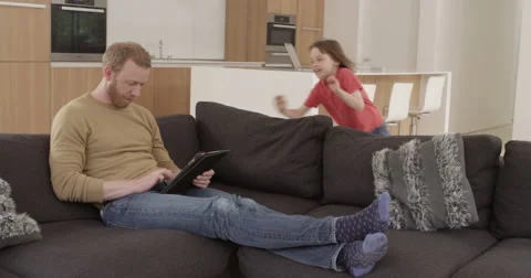 Girl dives onto sofa to look at tablet with dad in contemporary modern home, Stock Footage 50858717