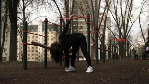 A girl does a forward tilt exercise on a sports field on the street Stock Footage 237991342