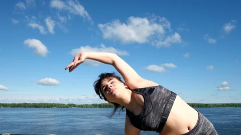 Girl does warm up and performing lateral tilts on the background of the river Stock Footage 76227193